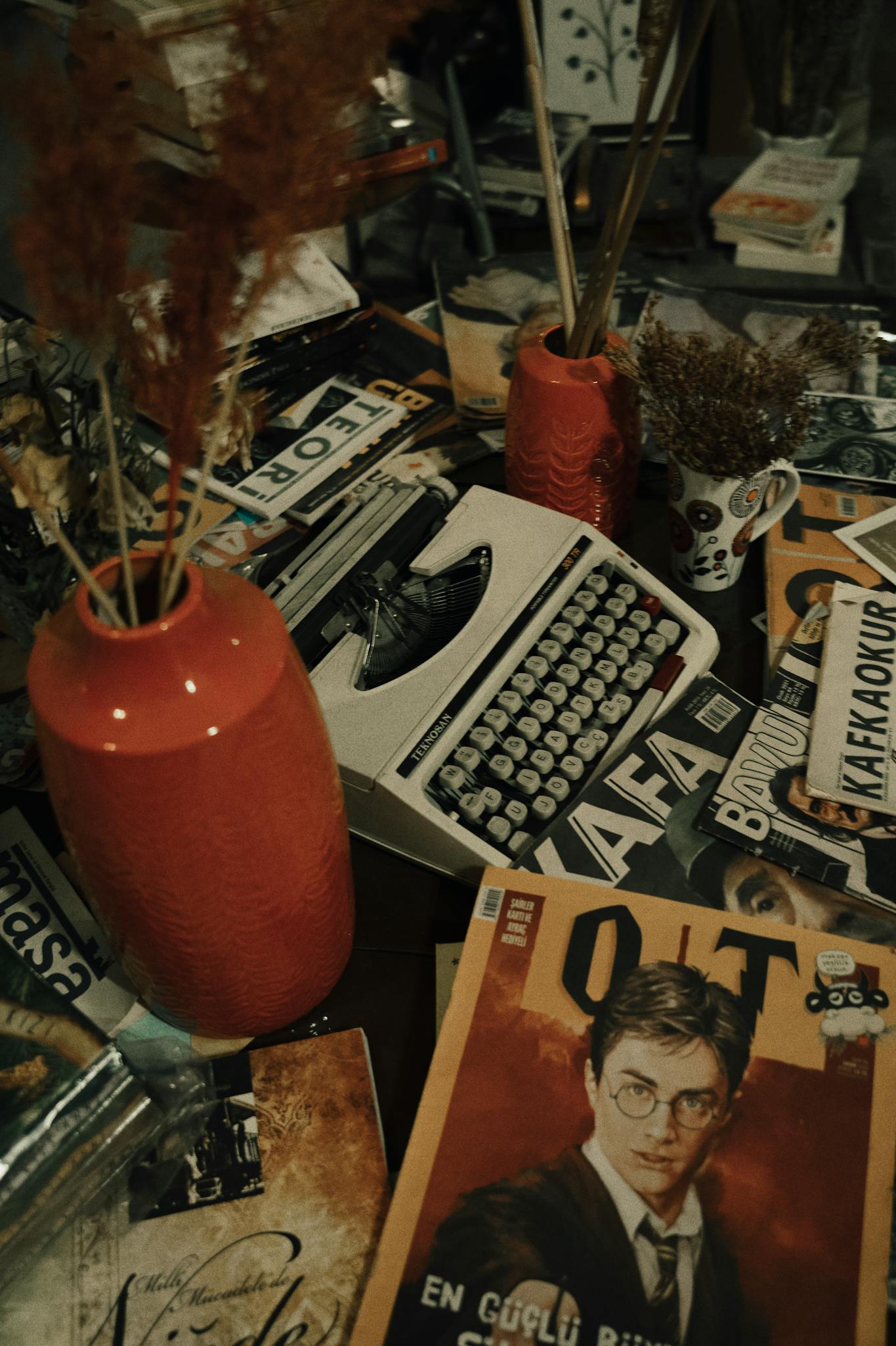 A cluttered desk with a vintage typewriter surrounded by magazines and decorative items.